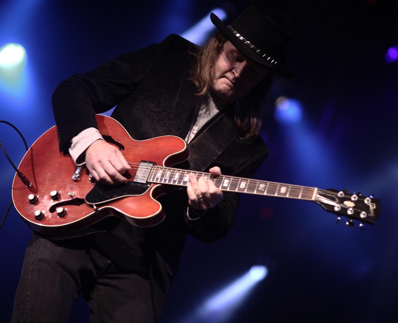 Rick Berthod playing his red Gibson guitar under blue stage lights